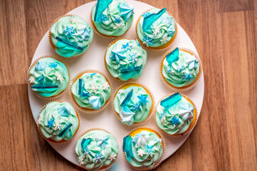 Homemade cupcake of blue color placed on wooden desk. Winter and christmas theme, snowflakes on cream with blue ice. Fresh and home baked sweet.