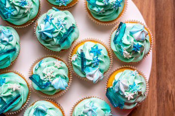 Homemade cupcake of blue color placed on wooden desk. Winter and christmas theme, snowflakes on cream with blue ice. Fresh and home baked sweet.