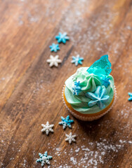 Obraz na płótnie Canvas Homemade cupcake of blue color placed on wooden desk. Winter and christmas theme, snowflakes on cream with blue ice. Fresh and home baked sweet.