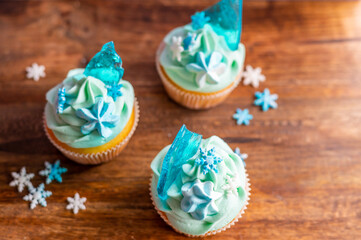 Homemade cupcake of blue color placed on wooden desk. Winter and christmas theme, snowflakes on cream with blue ice. Fresh and home baked sweet.