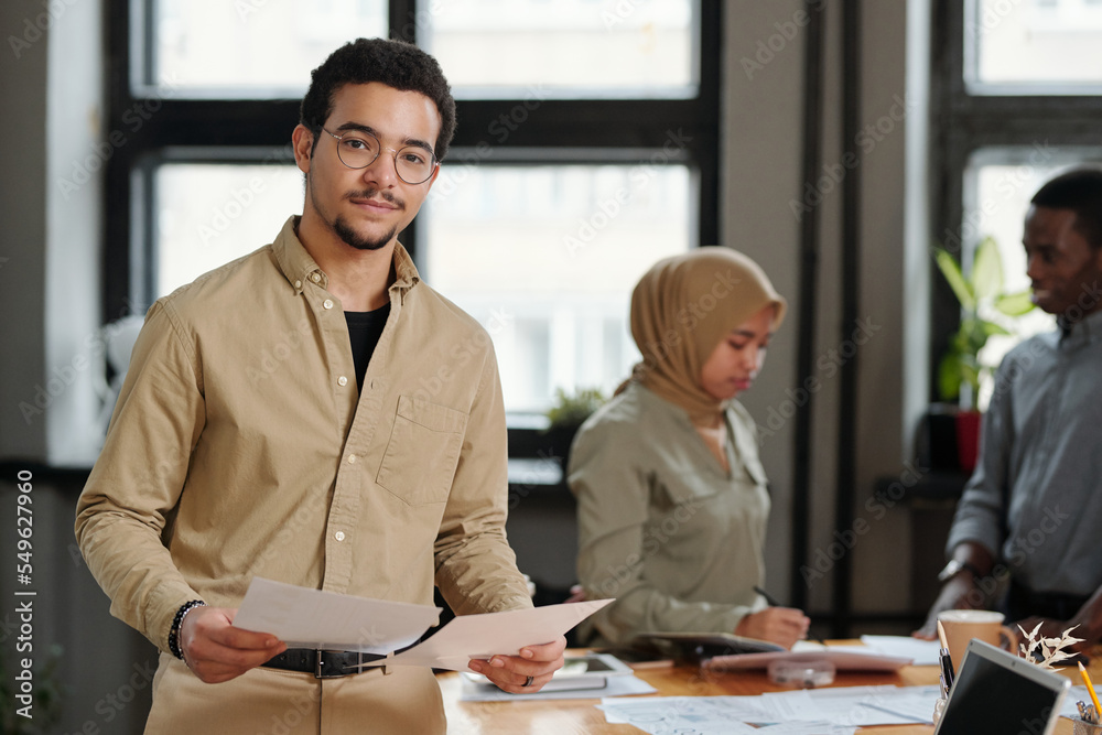 Aufkleber young confident broker with financial documents standing in front of camera in office and looking at
