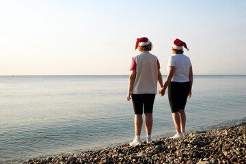 Funny Couple of women in santa claus hats on the sea beach, silhouette women as Santa hats hold hands on the seashore and wish merry christmas and happy new year.