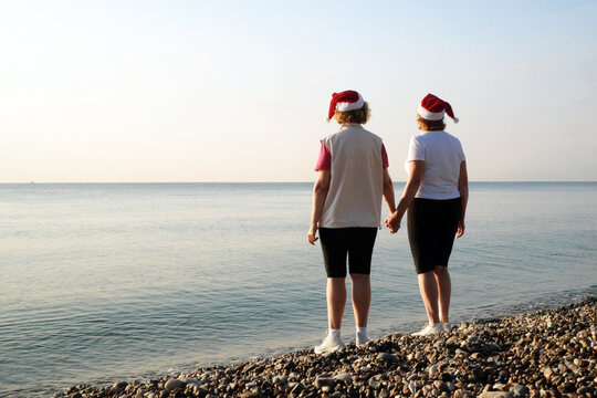 Funny Couple of women in santa claus hats on the sea beach, silhouette women as Santa hats hold hands on the seashore and wish merry christmas and happy new year.