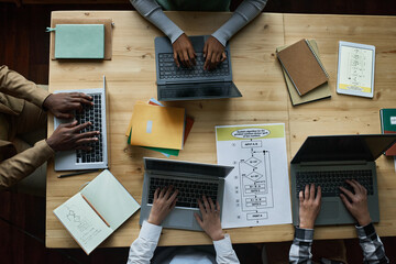 High angle view of teacher sitting at wooden table together with children at IT lesson, they typing on laptop computers to develop new software in team