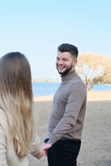 Fototapeta na wymiar Young man and woman holding hands and posing on the beach. The guy looks at the girl and smiles