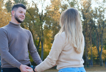 Young man and woman hold hands and look at each other. Boy and girl posing against the backdrop of autumn trees