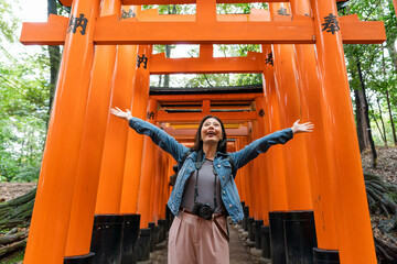 Fototapeta na wymiar cheerful Asian Japanese woman visitor standing in the middle of senbon torii gateway with spreading arms to embrace nature in the mountains in Kyoto japan. translation: âdedicationâ