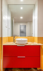 New empty bathroom with yellow tiles and round sink on red furniture