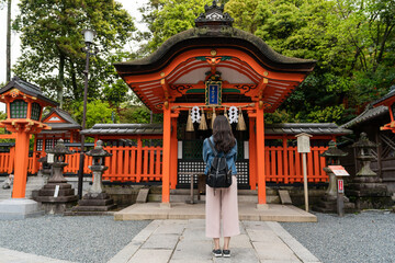 rear view with full length of devout asian Japanese woman standing and praying in front of red Shinto shrine at Fushimi Inari Taisha shrine in Kyoto japan at springtime