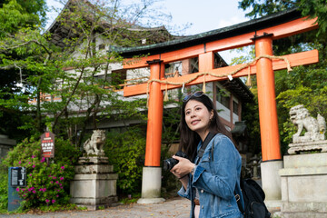 cheerful asian Japanese girl photographer looking into distance at beautiful scenery near the red torii gate of uji jinja while traveling to Kyoto japan during spring season