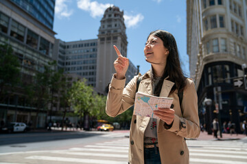 cheerful asian Japanese woman visitor looking at landmark in space with finger pointing gesture...