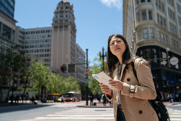 curious asian Japanese girl visitor looking around city with guide map while exploring downtown san Francisco in California usa near triangular office building on sunny day