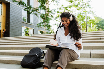 Young woman using cellphone and headphones while studying outdoors