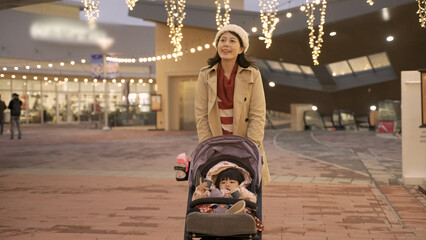 cheerful asian mother taking evening walk with her baby daughter in the pushchair outside a...