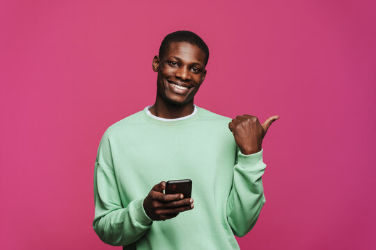 Black young man using cellphone and pointing finger aside