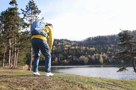 Tired male traveler with heavy backpack bending over near forest lake back view