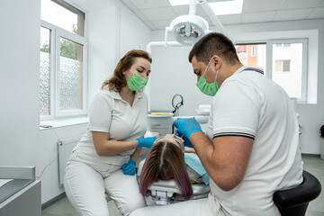 two dentists man woman treat the sick teeth of female patient who keeps her mouth open.