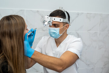 Naklejka premium An ENT specialist in a mask examines a patient's sore throat in the office.