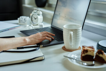 Hand of unrecognizabled person using laptop at workplace near window. Comfortable remote work at home
