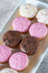 Cupcakes, decorated with icing and sprinkles on a white serving plate. On a concrete background