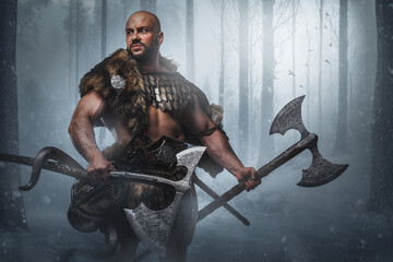 Studio shot of viking dressed in armor and fur holding two axes in frost wood.