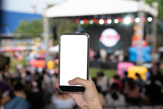 Hand holding mobile smartphone mock up white screen blank on music festival in the garden background.