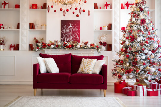 Interior of bright modern living room with fireplace, chandelier and comfortable sofa decorated with Christmas tree and red gifts