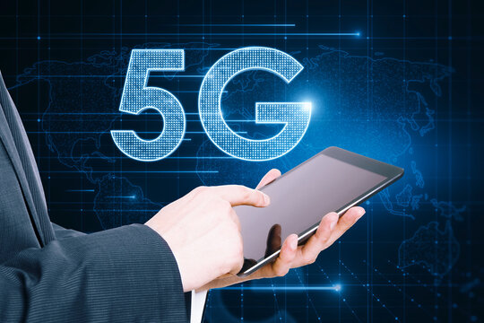 Close up of businessman hand pointing at tablet with glowing 5G hologram on blurry background. Wireless internet and web speed concept.