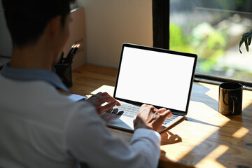 Over shoulder view of focused male office worker using laptop computer in bright office. Empty screen for advertise design