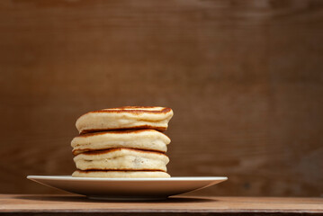 A stack of pancakes in a plate on a table on a dark wooden background.