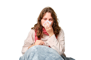 A sick woman blows her nose in a napkin, a runny nose, isolated on a white background. Adult ill woman with a red scarf sitting on a home bed in a white bedroom, female aged 35 years - obrazy, fototapety, plakaty
