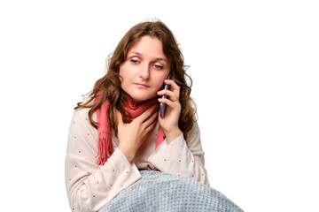 A sick woman is holding a sore throat with a phone in her hand, neck pain, isolated on a white background. Adult ill woman sitting on a home bed in a white bedroom, female aged 35 years
