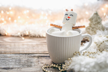 Close up, mug of hot drink with marshmallow snowman on blurred background.