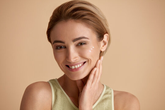 Skin Care Woman Posing with Cream on Cheek. Closeup Of Beautiful Smiling Girl with Moisturizer On Fresh Soft Pure Skin. Portrait Of Woman With Natural Makeup Recommended Beauty Cosmetics Product 