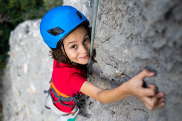 child rock climber in a blue protective helmet overcomes the route in the mountains. children's sports in nature.