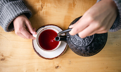 Woman in a cafe pour tea from a black cast iron teapot, top view.