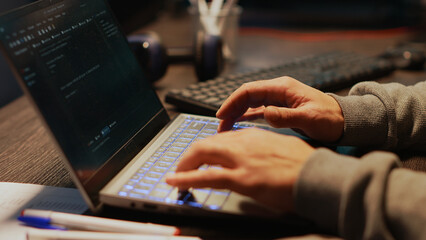 Young man hacking password to break server security, using virus to infect laptop and steal big data. Dangerous mysterious hacker typing code to do cyber attack on system database. Close up.