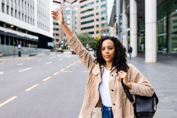 Woman standing on footpath hailing taxi in city
