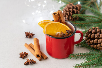 Seasonal hot drink with spices and orange slices in red mug on light background with fir branches. Mulled wine, punch or sangria for winter holidays