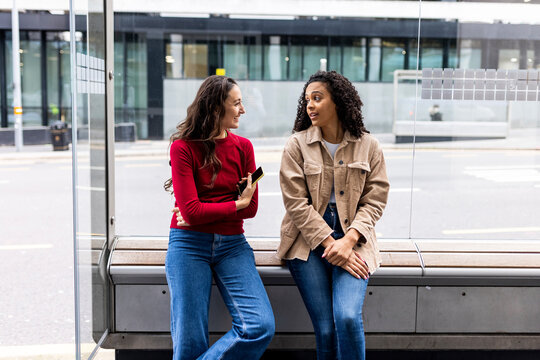 Woman talking with friend sitting at bus stop
