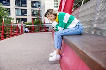 Sad young woman with headphones sitting on bench