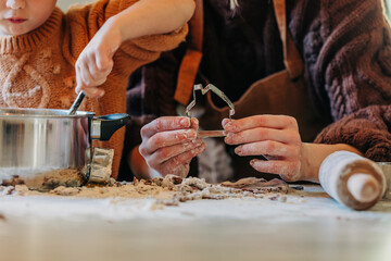 Boy cooking with mother holding house shaped cookie cutter at table