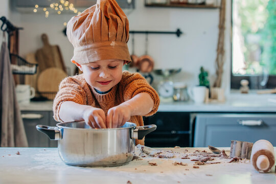 Smiling boy wearing chefs hat preparing food in utensil at home
