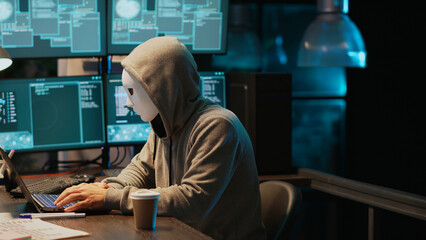 Cyber terrorist with mask hacking database servers, hacker with hood on hacking computer system and...