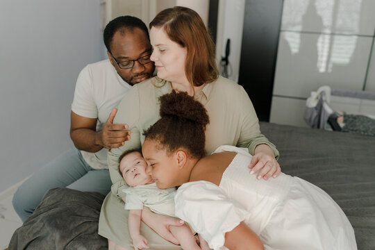 Loving father and mother with daughter embracing baby girl at home