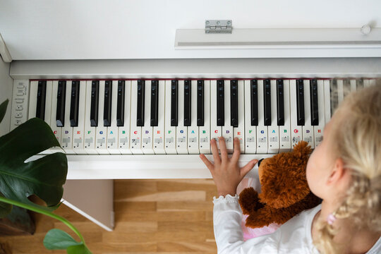 Girl with teddy bear learning piano at home