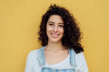Beautiful smiling woman with curly hair in front of yellow wall