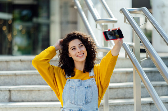 Smiling young woman with hand in hair taking selfie through mobile phone on staircase