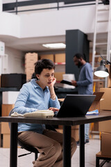 Storehouse employee sitting at desk table analyzing customer shipping detalies on laptop computer before start preparing package, working on delivery in warehouse. Distribution center company