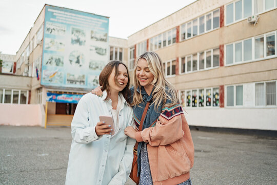 Happy mother and daughter sharing smart phone standing on schoolyard